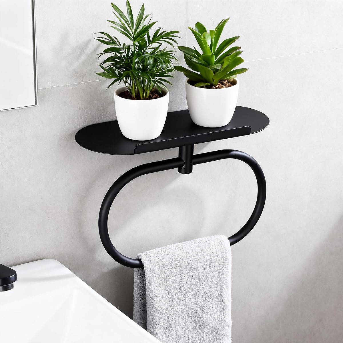 Anneau porte-serviettes mural noir avec tablette ovale, fixé sur un mur minéral clair dans une salle de bain lumineuse.