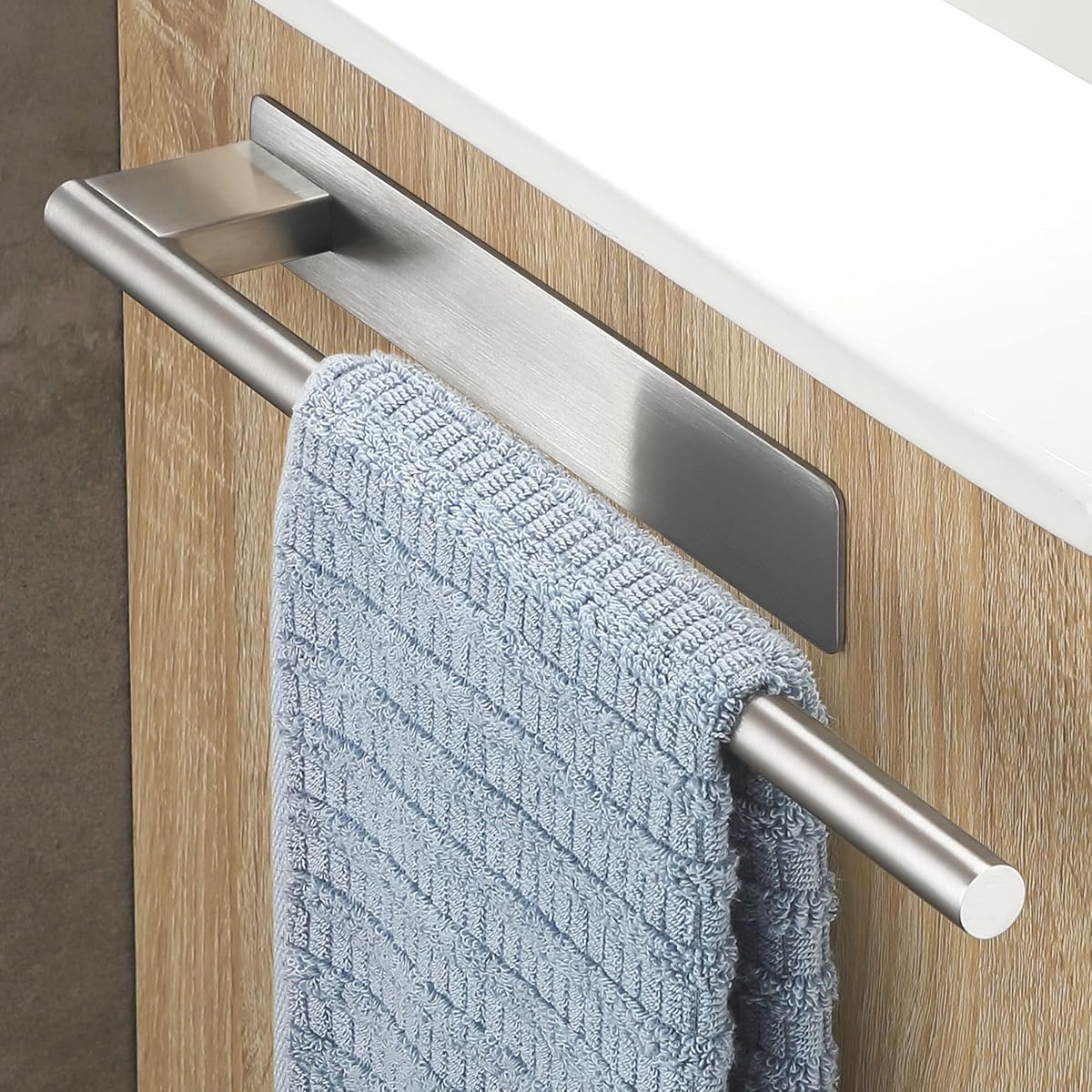 Barre porte-serviettes adhésive argentée brossée avec deux serviettes dans une salle de bain lumineuse